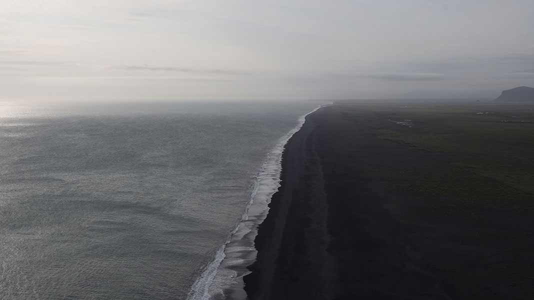 Moody Icelandic Photograph Showing a Diagonal Surf Line Center with Ocean to the Left and Black Sand Beach to the Right.